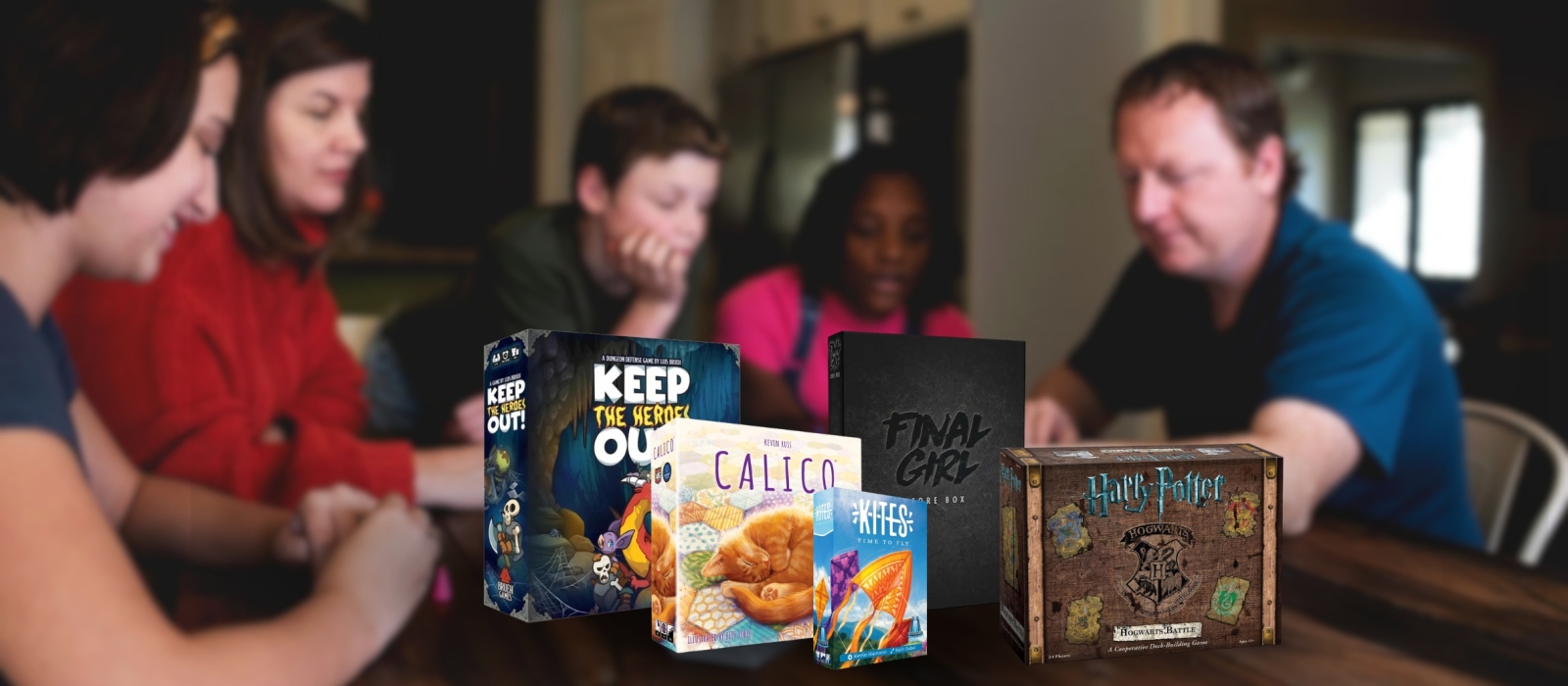 In the background people are playing a game and are laughing. In the front the board games and card games Keep The Heroes Out!, Calico, Kites, Final Girl Core Box, and Harry Potter Hogwarts Battle.