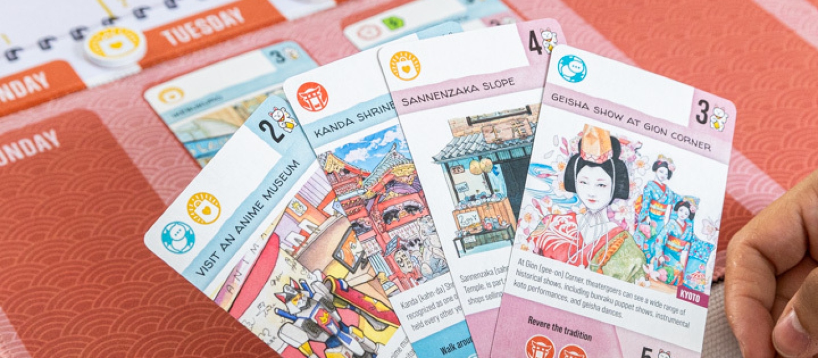Close-up of Let's Go! To Japan board game, featuring a hand holding cards with the game board in the background.
