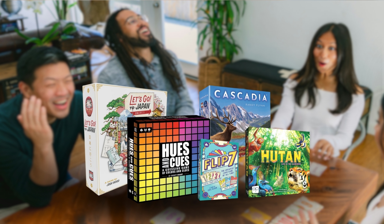 In the background people are playing a game and are laughing. In the front the board games and card games Let's Go! To Japan, Hues and Cues, Flip 7, Cascadia, and Hutan.