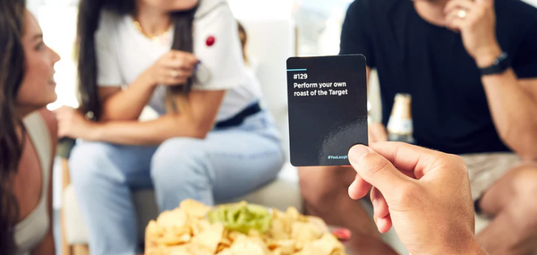 People playing the game You Laugh You Drink with smiles and laughing during a game night